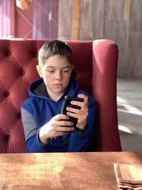 Portrait of boy with a phone sitting nearby table