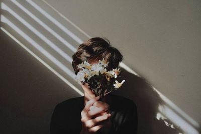 Portrait of woman holding flower against wall