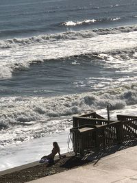 Man sitting on beach by sea against sky