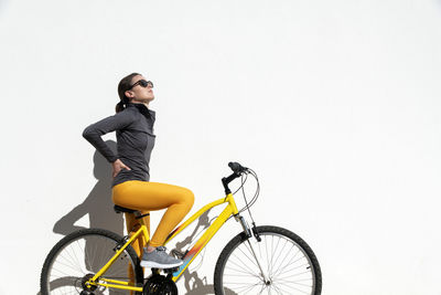 Portrait of young woman riding bicycle against wall