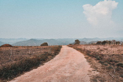 Dirt road amidst field against sky