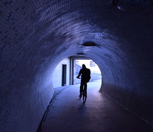Rear view of person riding bicycle through tunnel