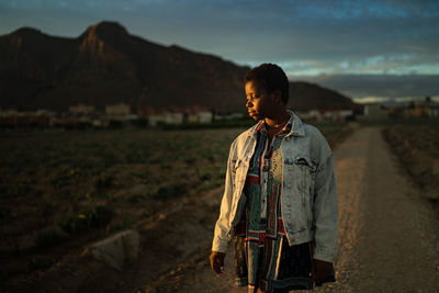 Woman standing on land against sky during sunset