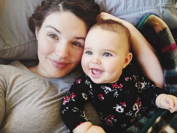 Portrait of mother lying with cheerful toddler daughter on bed