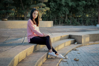 Portrait of young woman sitting on footpath