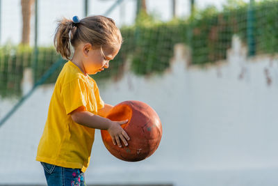 Cute little girl in yellow t-shirt holding ball in her hands and going to kick it