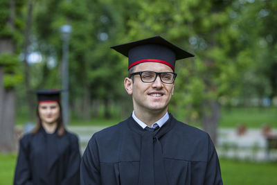 Friends in graduation gown standing against trees