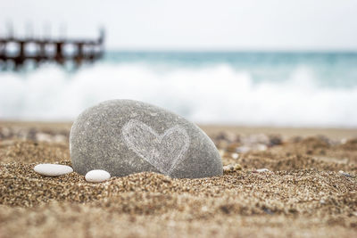 Round stone with a heart symbol lies on the golden sand of the beach on a blurred background of sea