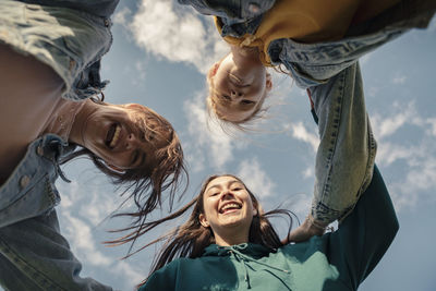 Smiling female friends looking down against sky on sunny day