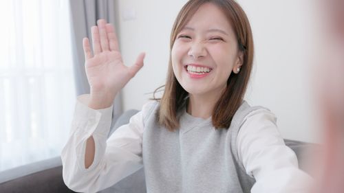 Portrait of smiling young woman gesturing against wall