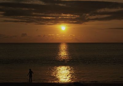 Silhouette man standing on beach against sky during sunset