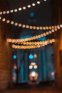 Defocused image of illuminated string lights hanging at alley