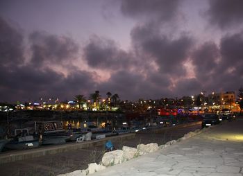 Illuminated city against cloudy sky at night