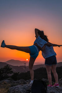 Friends standing on mountain against clear sky at sunset