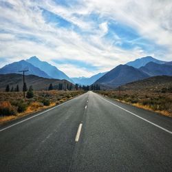 Empty road by mountains against cloudy sky