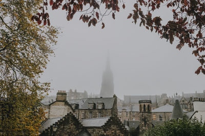 Amazing view of ancient scottish city inverness with stone houses and high church building covered with fog framed by branches of colorful autumn trees