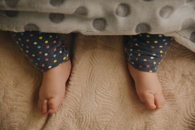 Low section of baby feet lying on bed under blanket 