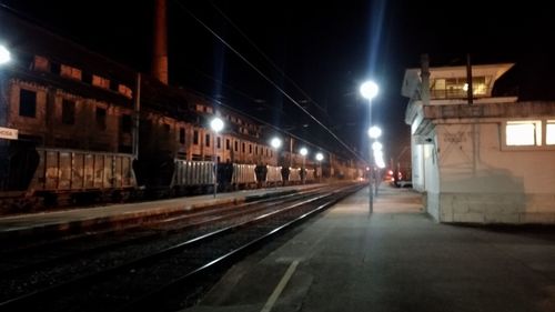 Illuminated railroad tracks amidst buildings in city at night