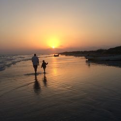 Silhouette people on beach against sky during sunset