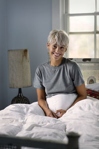 Portrait of happy young woman sitting on bed at home