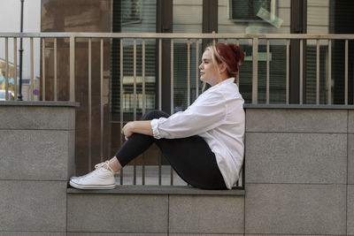 Young real beautiful brown haired woman in jeans and t-shirt sitting on stone steps, railing outdoor