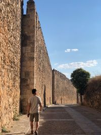 Full length rear view of man walking on footpath by historic building wall 