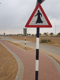 Road sign by street against sky