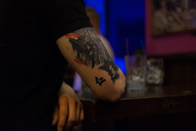 Midsection of man with tattoo sitting in restaurant