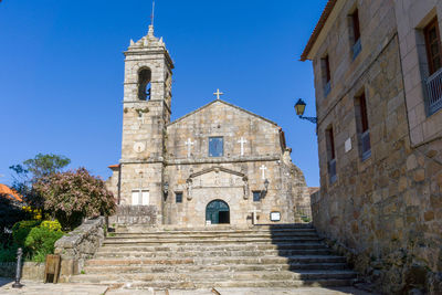 Low angle view of cross amidst buildings against clear blue sky