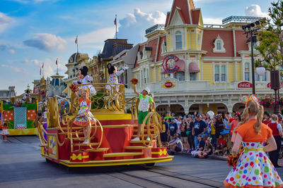 People in amusement park by buildings against sky in city