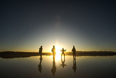 Silhouette people by lake against sky during sunset