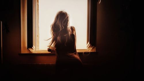 Rear view of woman looking through window at home