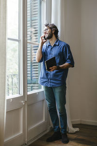 Businessman standing at office window, using smart phone