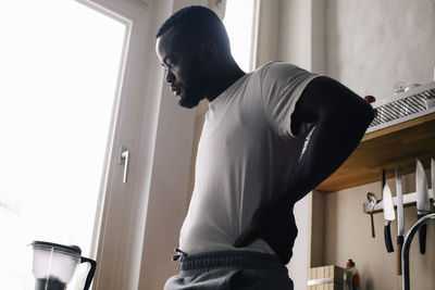 Emotionally depressed lonely man standing with hand on hip in kitchen