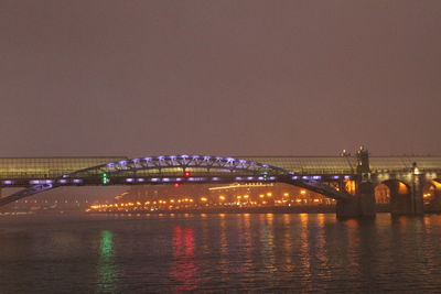 Illuminated bridge over river against sky at night