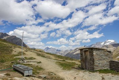 Trough and hut on mountain against cloudy sky