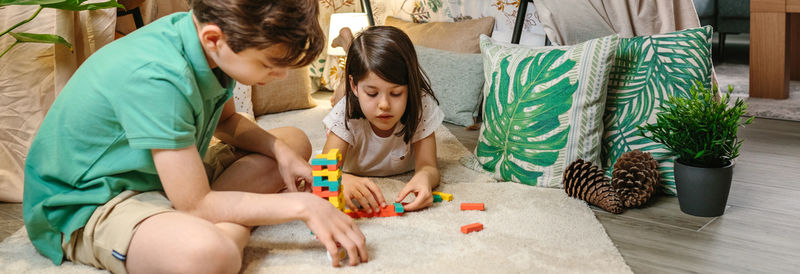 Banner of happy children playing together with stacking piece game in front of homemade tent at home
