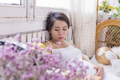 Close-up of pink flowers against pregnant woman sitting on bed at home