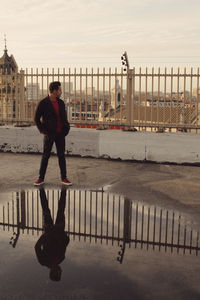 Full length portrait of young man standing by railing in city