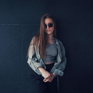 Beautiful young woman wearing sunglasses against wall