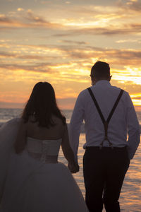 Rear view of couple standing on land during sunset