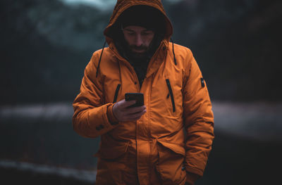 Man wearing jacket using smart phone while standing outdoors