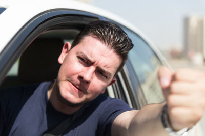 Frustrated man gesturing through window while traveling in car