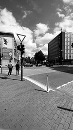 Man on footpath by street against sky in city