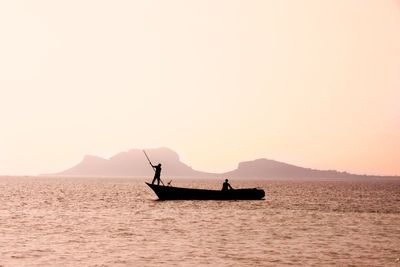 Silhouette people on boat in sea against clear sky