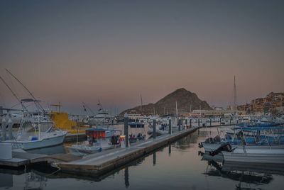 Boats moored in harbor at sunset