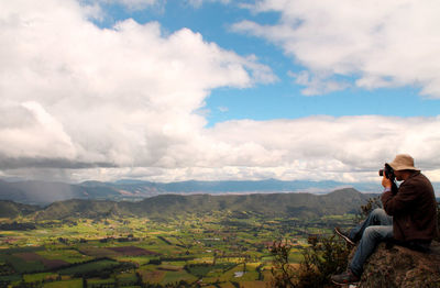 Woman sitting on mountain against sky