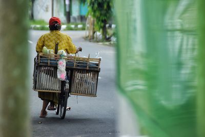 Rear view of vendor selling vegetables in basket on bicycle at city