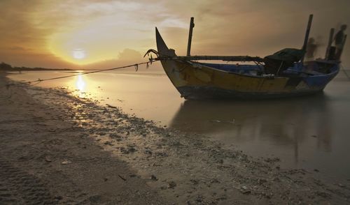 Boat moored on beach against sky during sunset