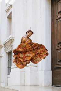 Happy young woman jumping in front of building